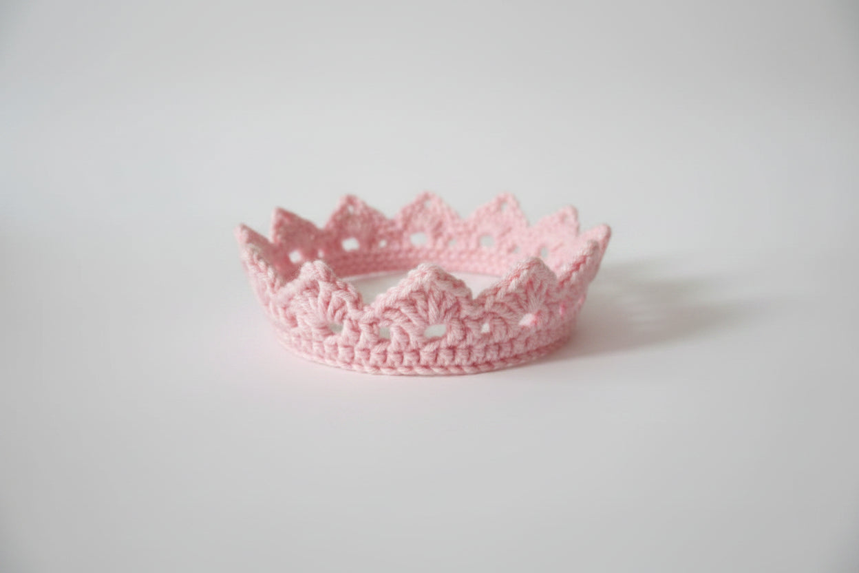 Pink crocheted crown on a light surface with a dark background