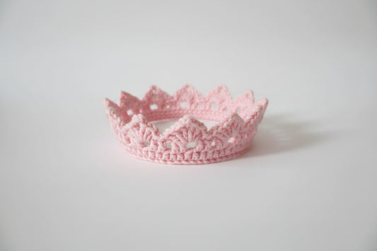Pink crocheted crown on a light surface with a dark background